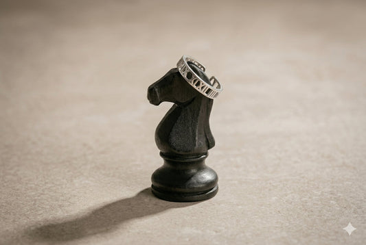 Sterling silver Roman numeral ring resting on black carved chess knight piece, editorial jewelry product photography | Glass Balloon