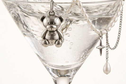 Sterling silver teddy bear charm pendant and pearl  beaded necklace draped over martini glass with water  splash, jewelry editorial - Glass Balloon