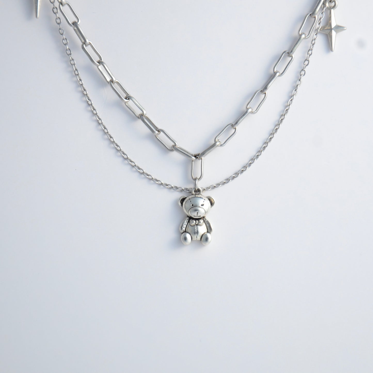 Silver chain charm necklace with a teddy bear pendant on a white background