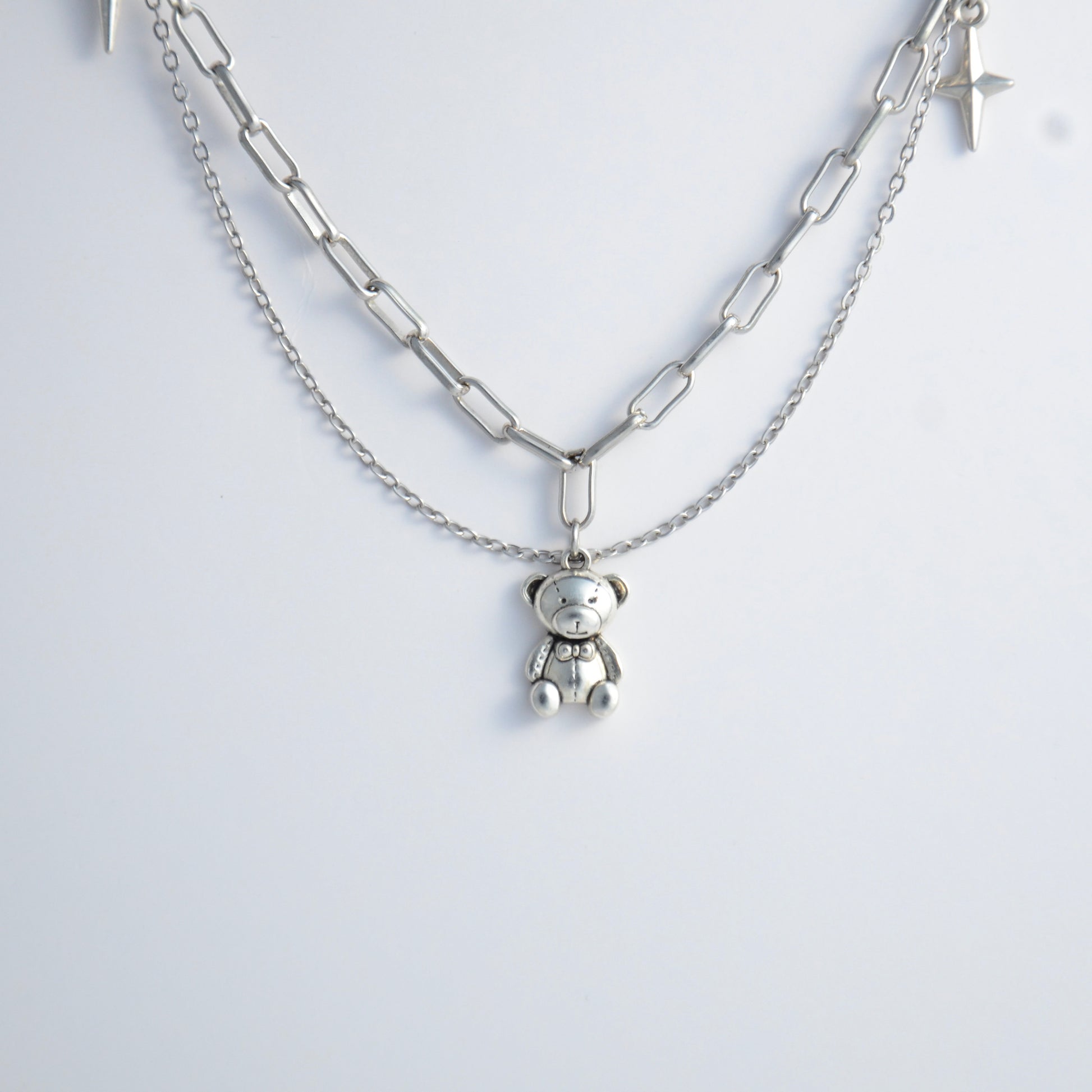 Silver chain charm necklace with a teddy bear pendant on a white background