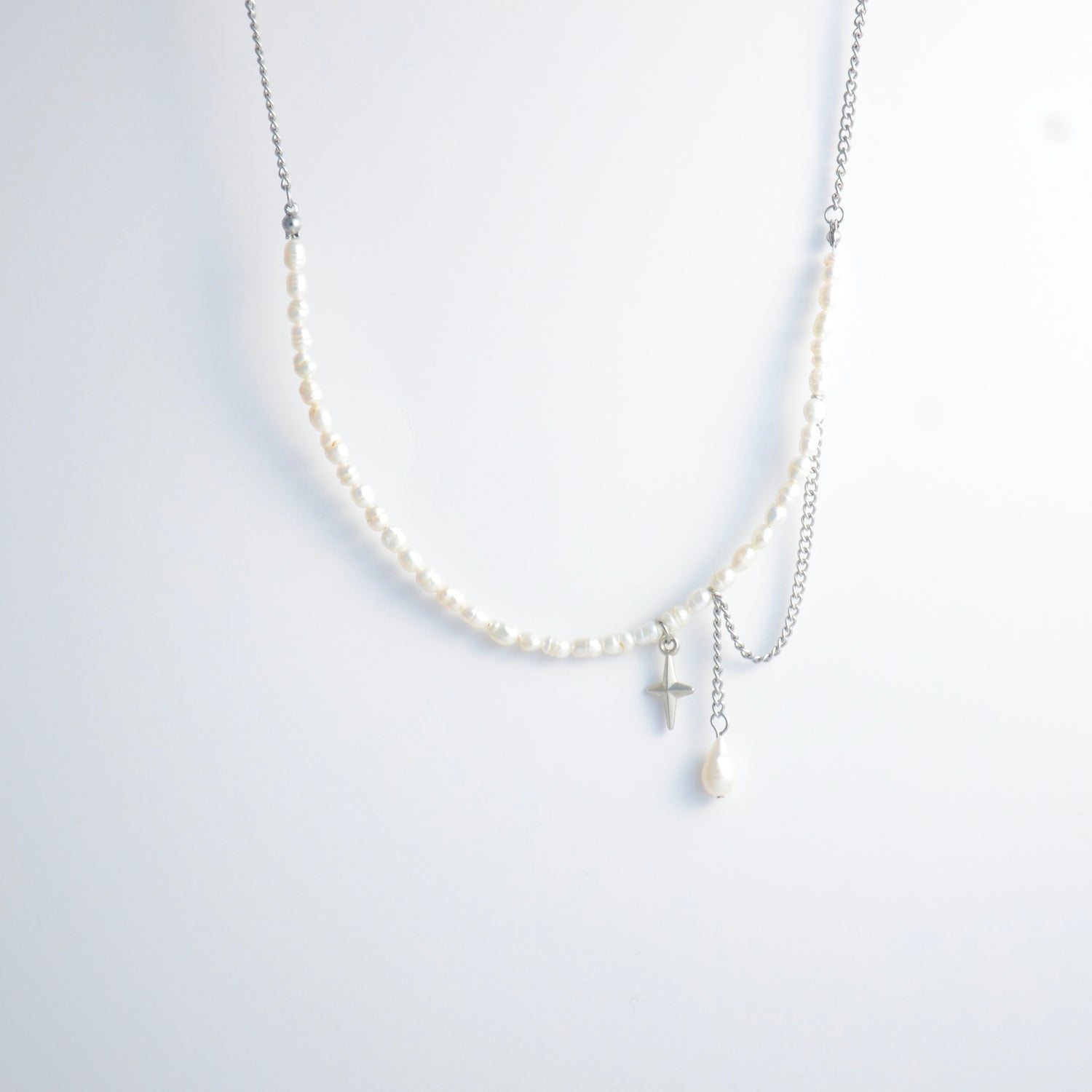 Pearl choker necklace with a small star pendant and a layering chain with pearl on a light gray background