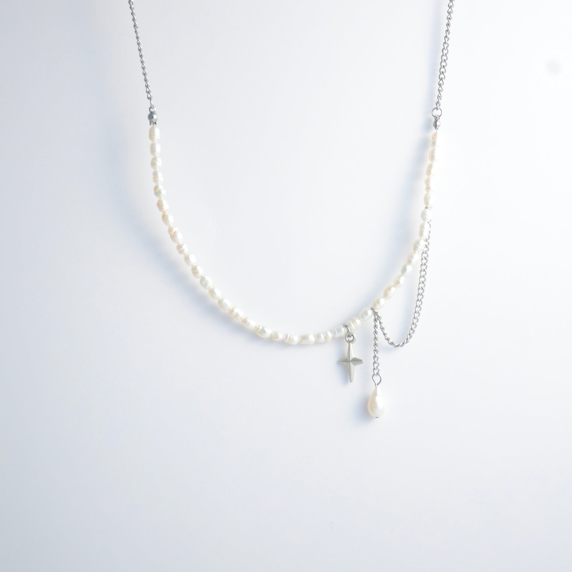 Pearl choker necklace with a small star pendant and a layering chain with pearl on a light gray background