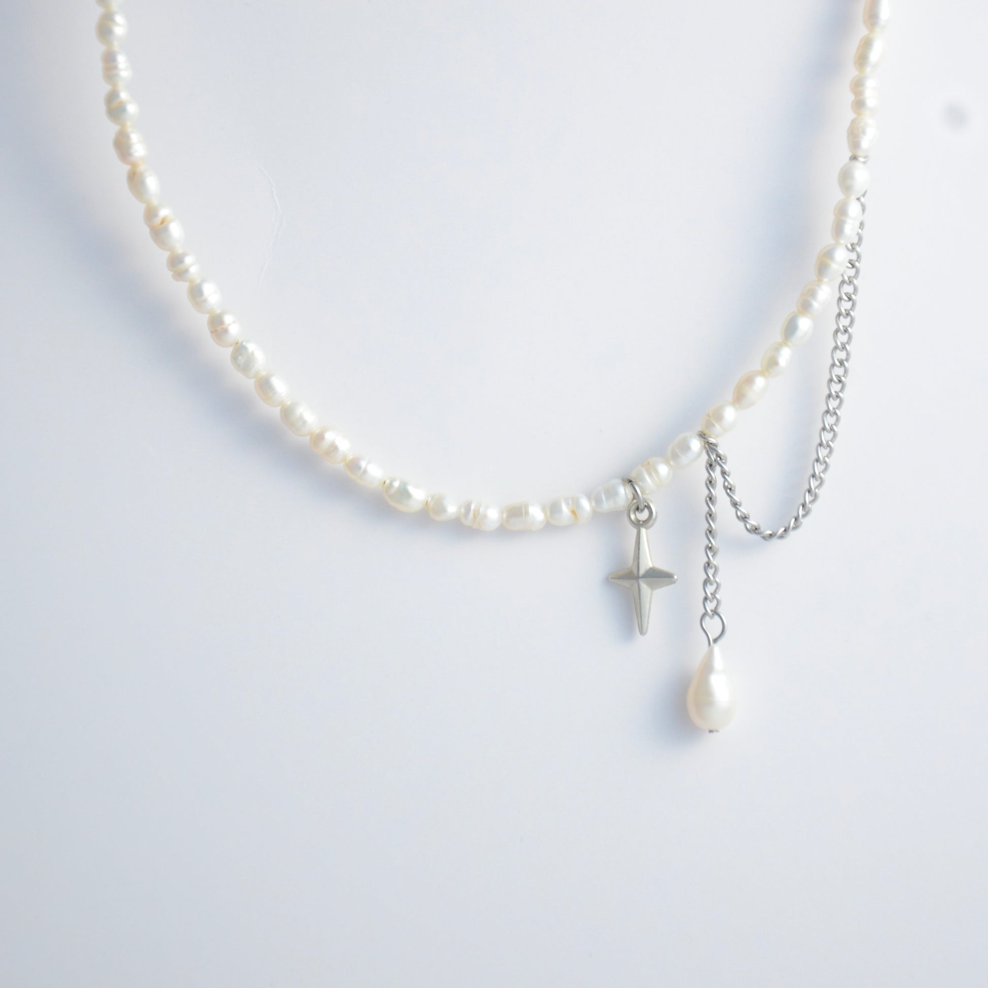 Pearl choker necklace with a small star pendant and a layering chain with pearl on a light gray background