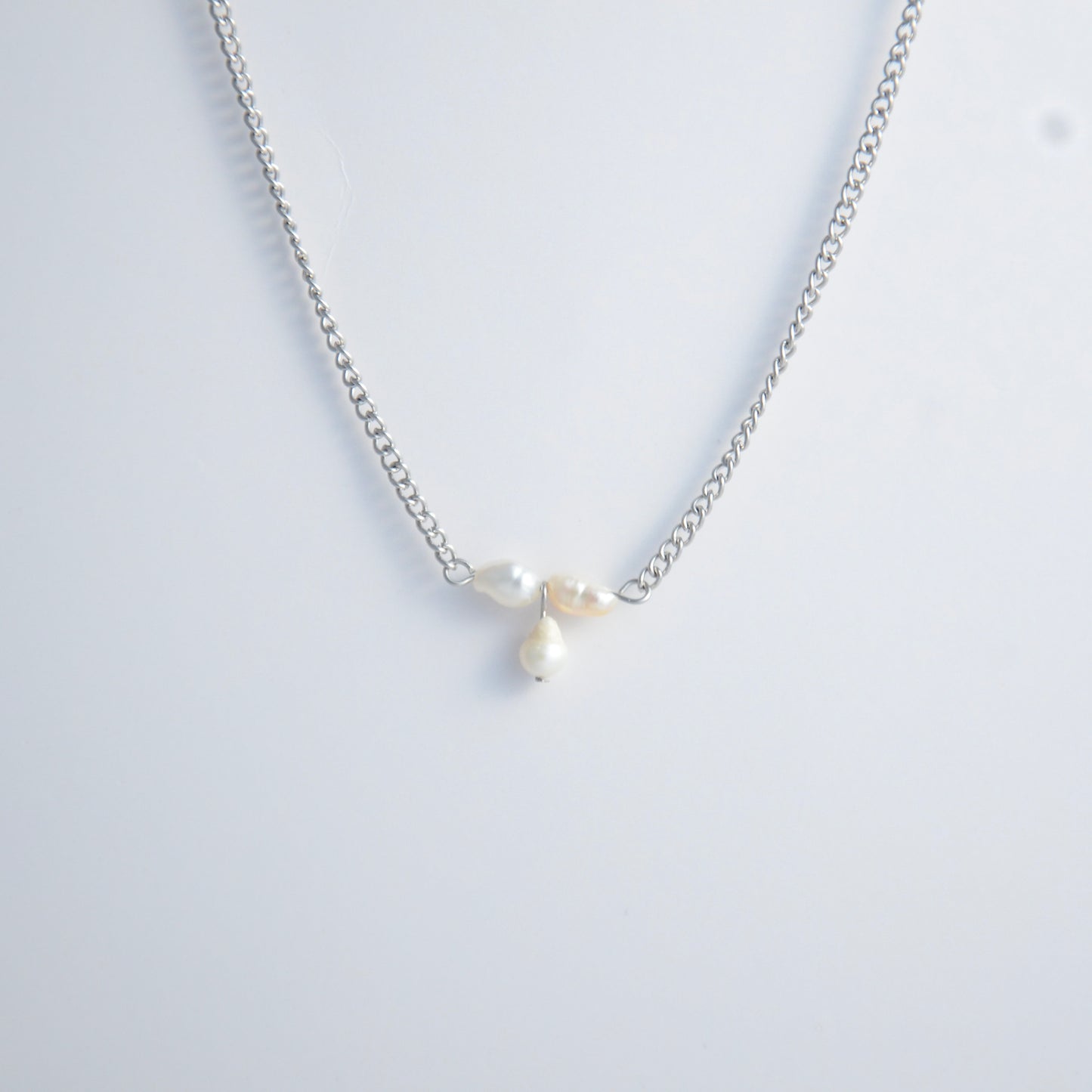 Silver necklace non-tarnish with three pearl beads on a light gray background