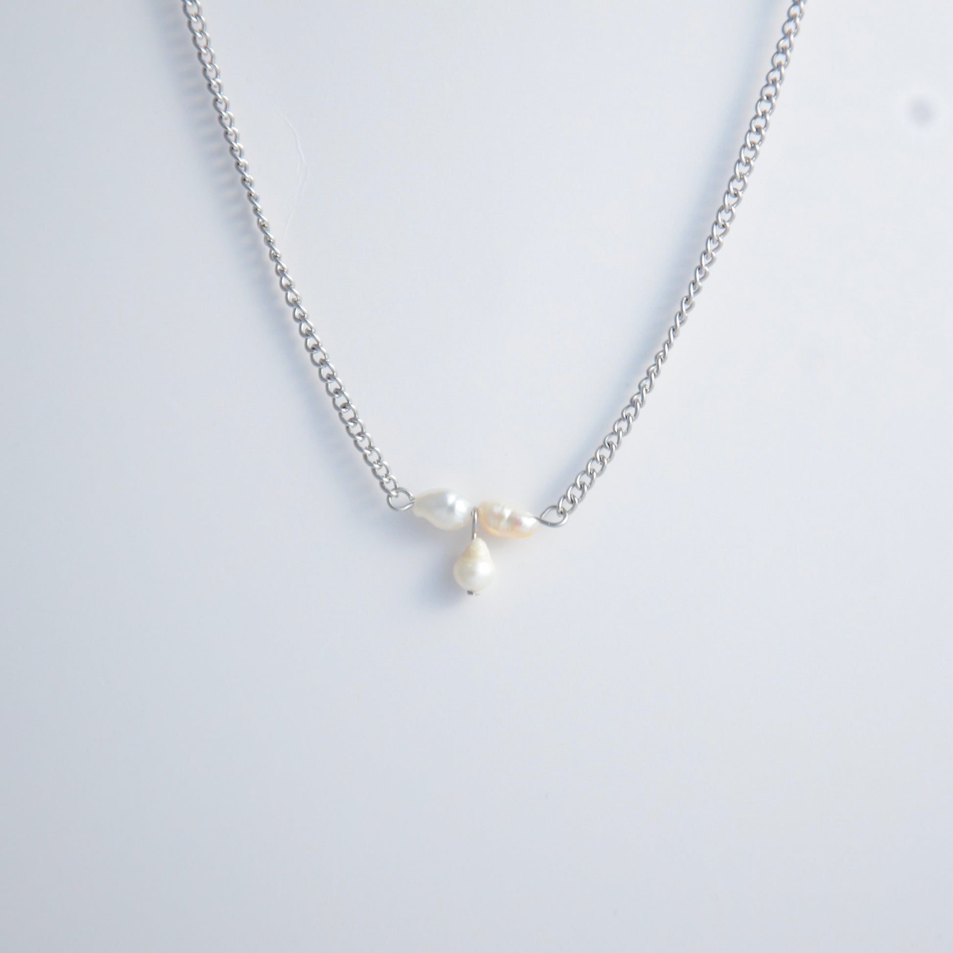 Silver necklace non-tarnish with three pearl beads on a light gray background