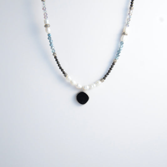 Silver beaded necklace with black pendant and multicolored beads on a light gray background