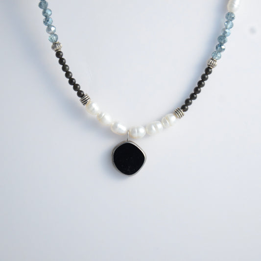 Silver beaded necklace with black pendant and multicolored beads on a light gray background