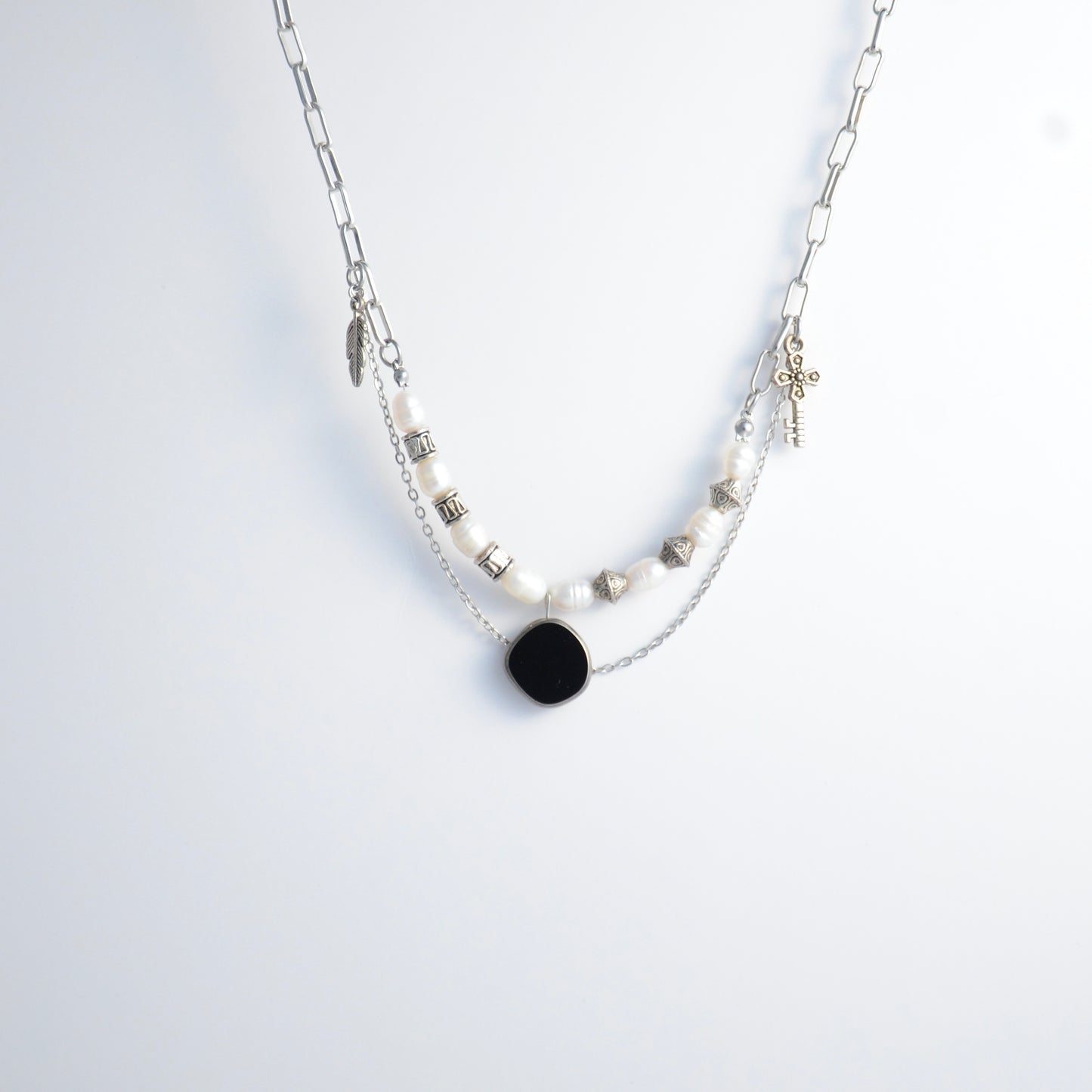 Silver charm necklace with black pendant and pearl-like beads on a white background