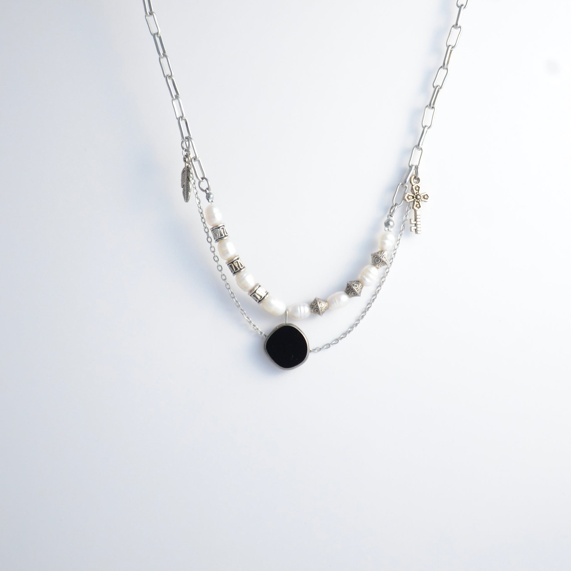 Silver charm necklace with black pendant and pearl-like beads on a white background
