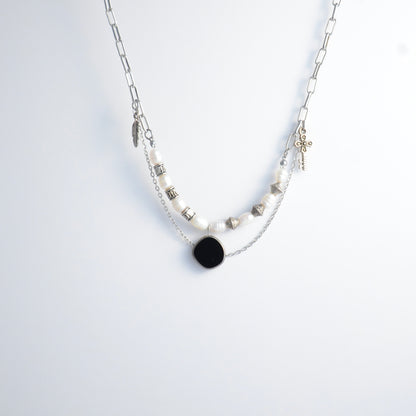 Silver charm necklace with black pendant and pearl-like beads on a white background