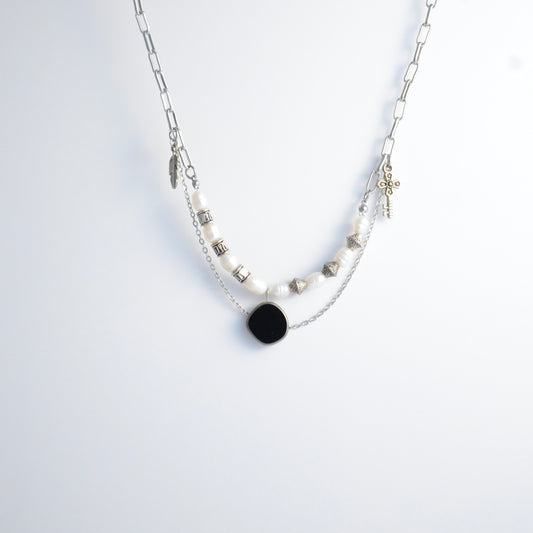 Silver charm necklace with black pendant and pearl-like beads on a white background