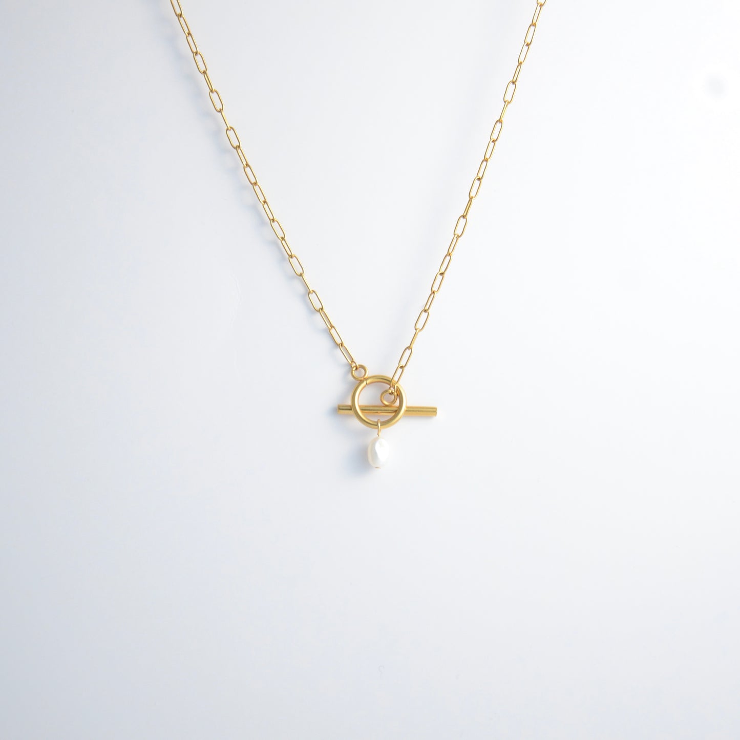Gold paperclip necklace with toggle clasp and a pearl pendant on a light gray background