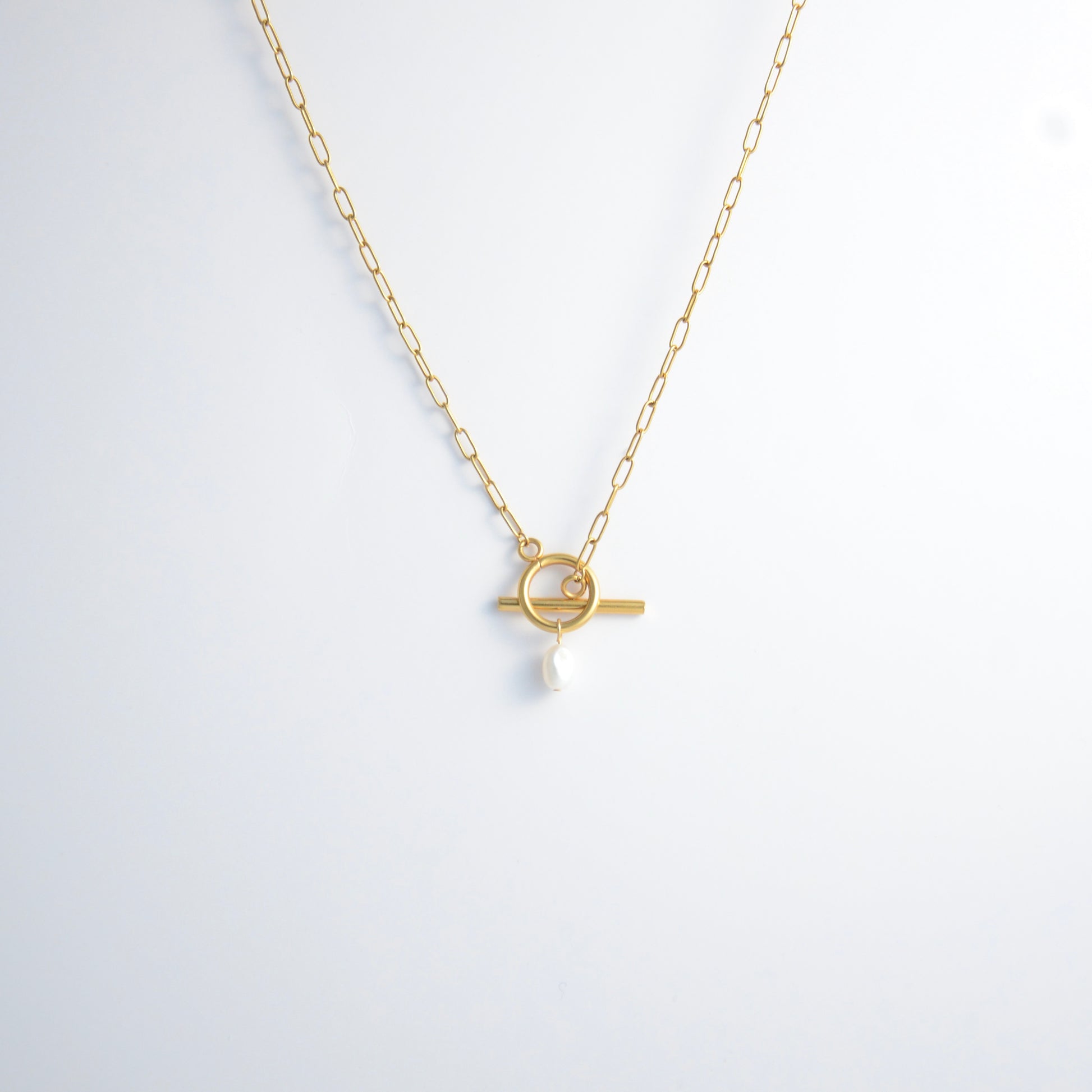 Gold paperclip necklace with toggle clasp and a pearl pendant on a light gray background
