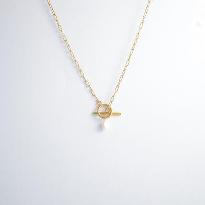 Gold paperclip necklace with toggle clasp and a pearl pendant on a light gray background