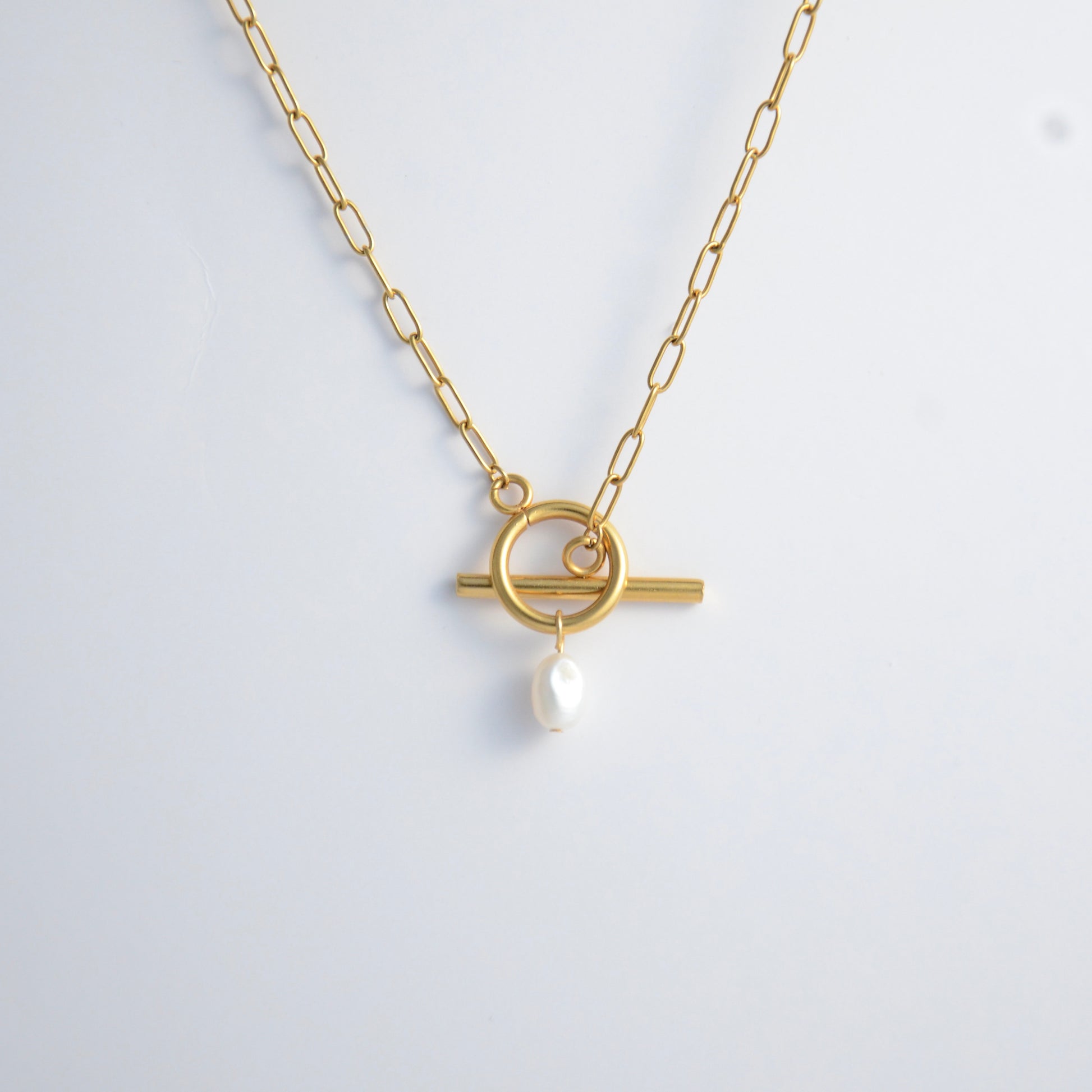 Gold paperclip necklace with toggle clasp and a pearl pendant on a light gray background