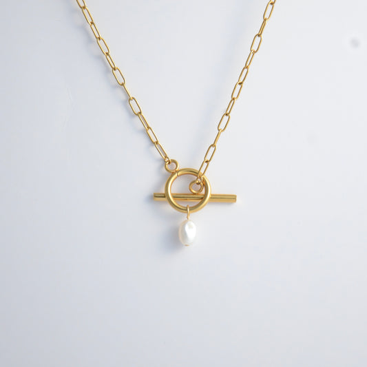 Gold paperclip necklace with toggle clasp and a pearl pendant on a light gray background