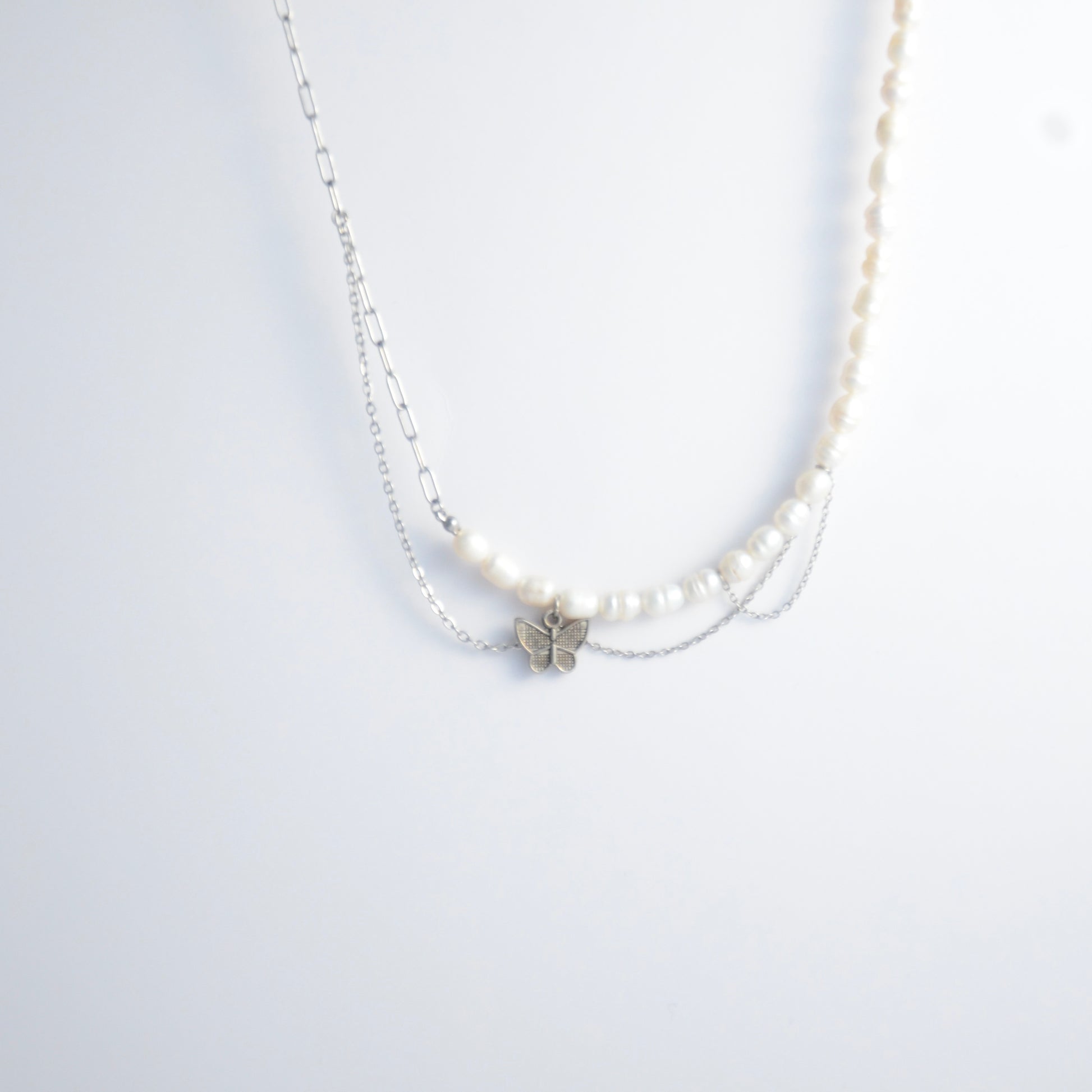 Silver necklace non-tarnish with pearl strands, layered chains and a silver butterfly pendant on a light gray background