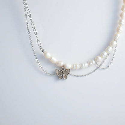Silver necklace non-tarnish with pearl strands, layered chains and a silver butterfly pendant on a light gray background