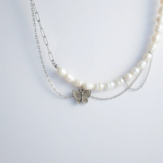 Silver necklace non-tarnish with pearl strands, layered chains and a silver butterfly pendant on a light gray background