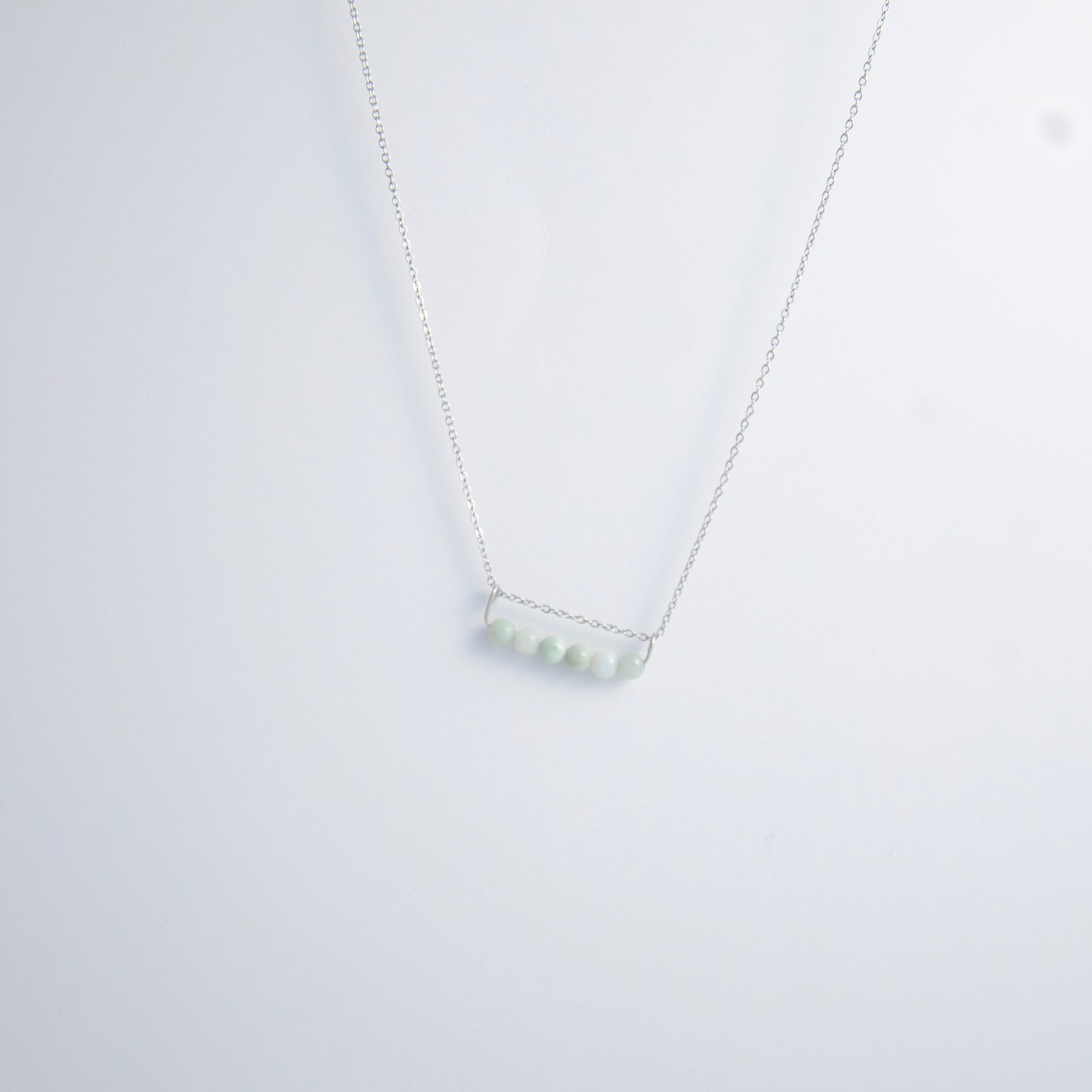Silver necklace with a pendant made of jade beads on a light gray background