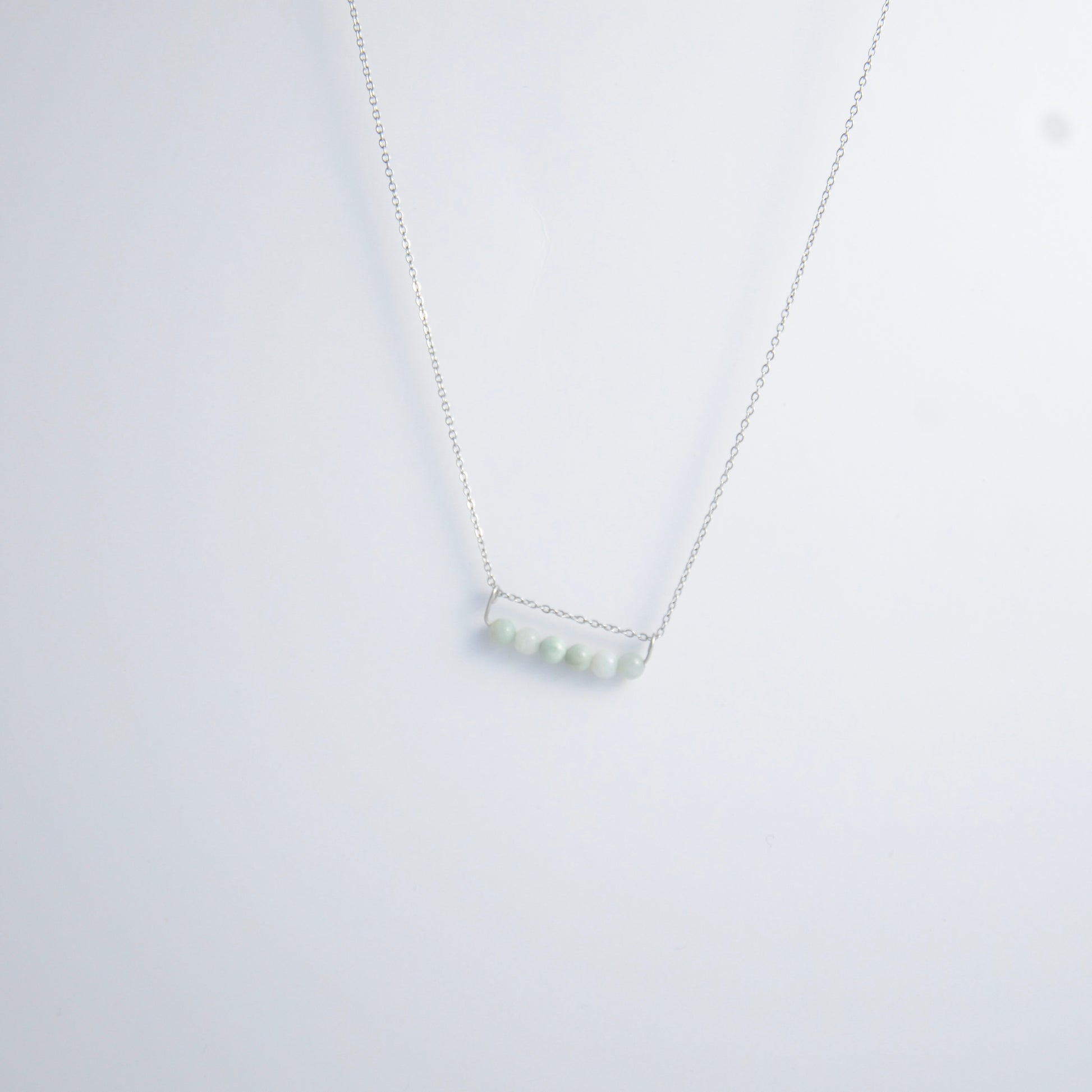 Silver necklace with a pendant made of jade beads on a light gray background
