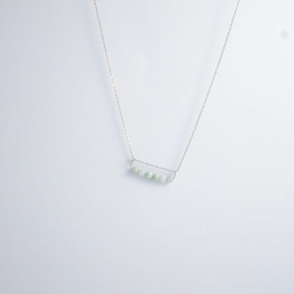 Silver necklace with a pendant made of jade beads on a light gray background