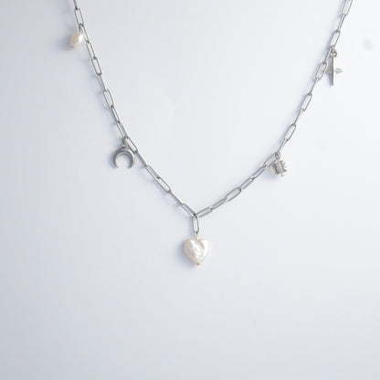 Silver chain charm necklace with pearl pendants, glass bead, and star pendants on a light gray background