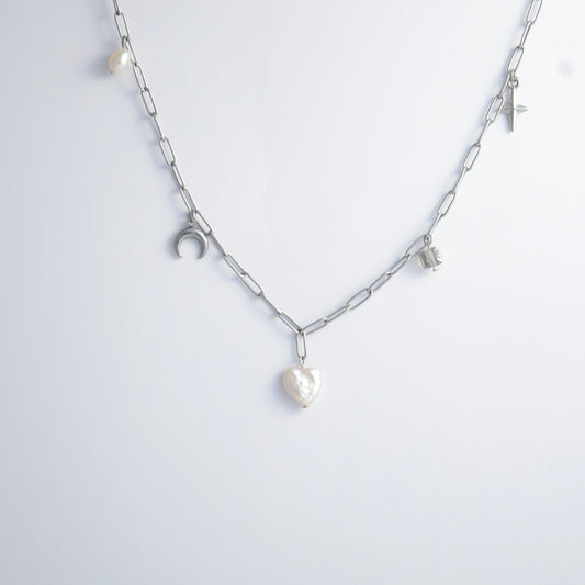 Silver chain charm necklace with pearl pendants, glass bead, and star pendants on a light gray background