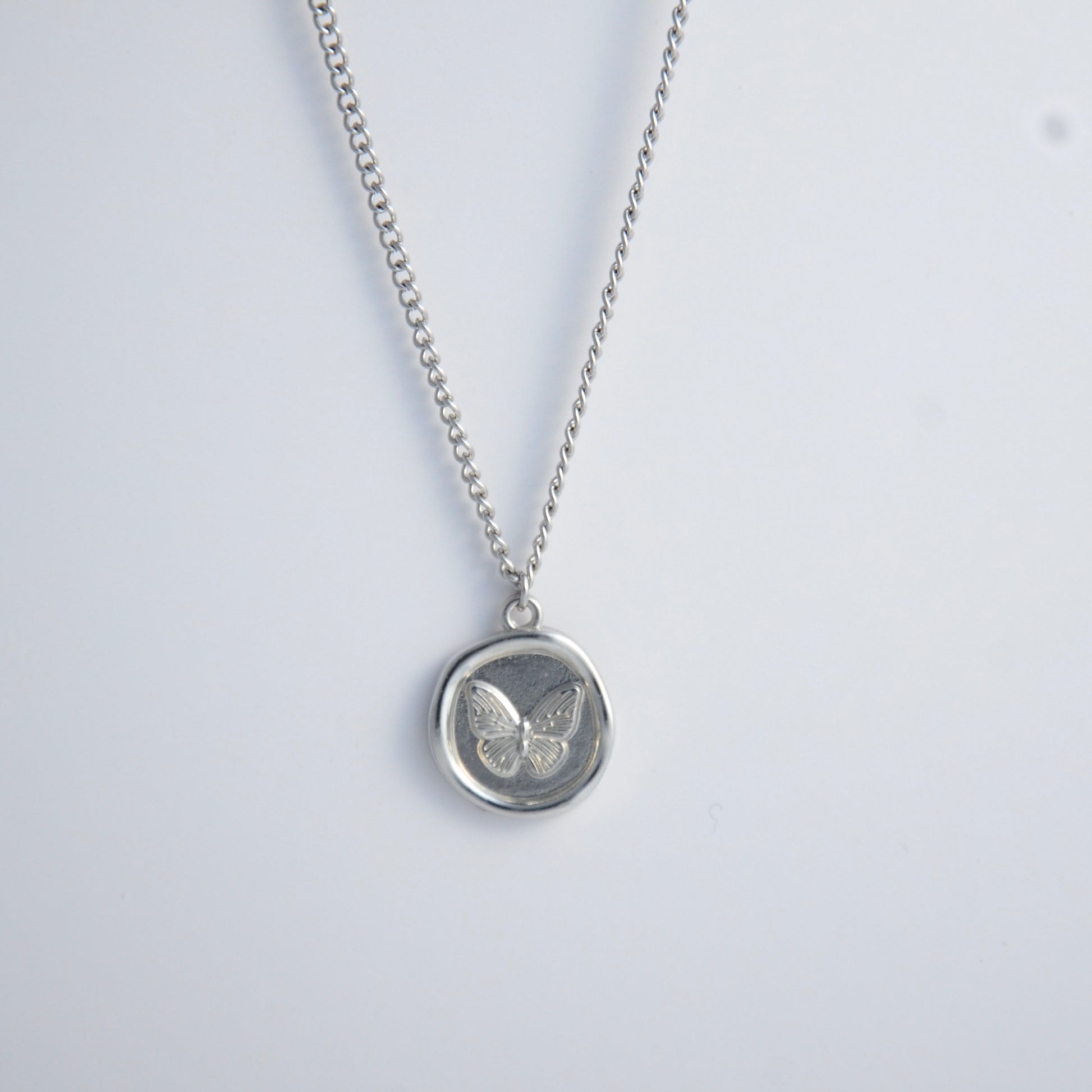 Silver curb necklace with a round butterfly pendant on a light gray background