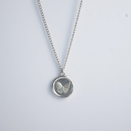 Silver curb necklace with a round butterfly pendant on a light gray background