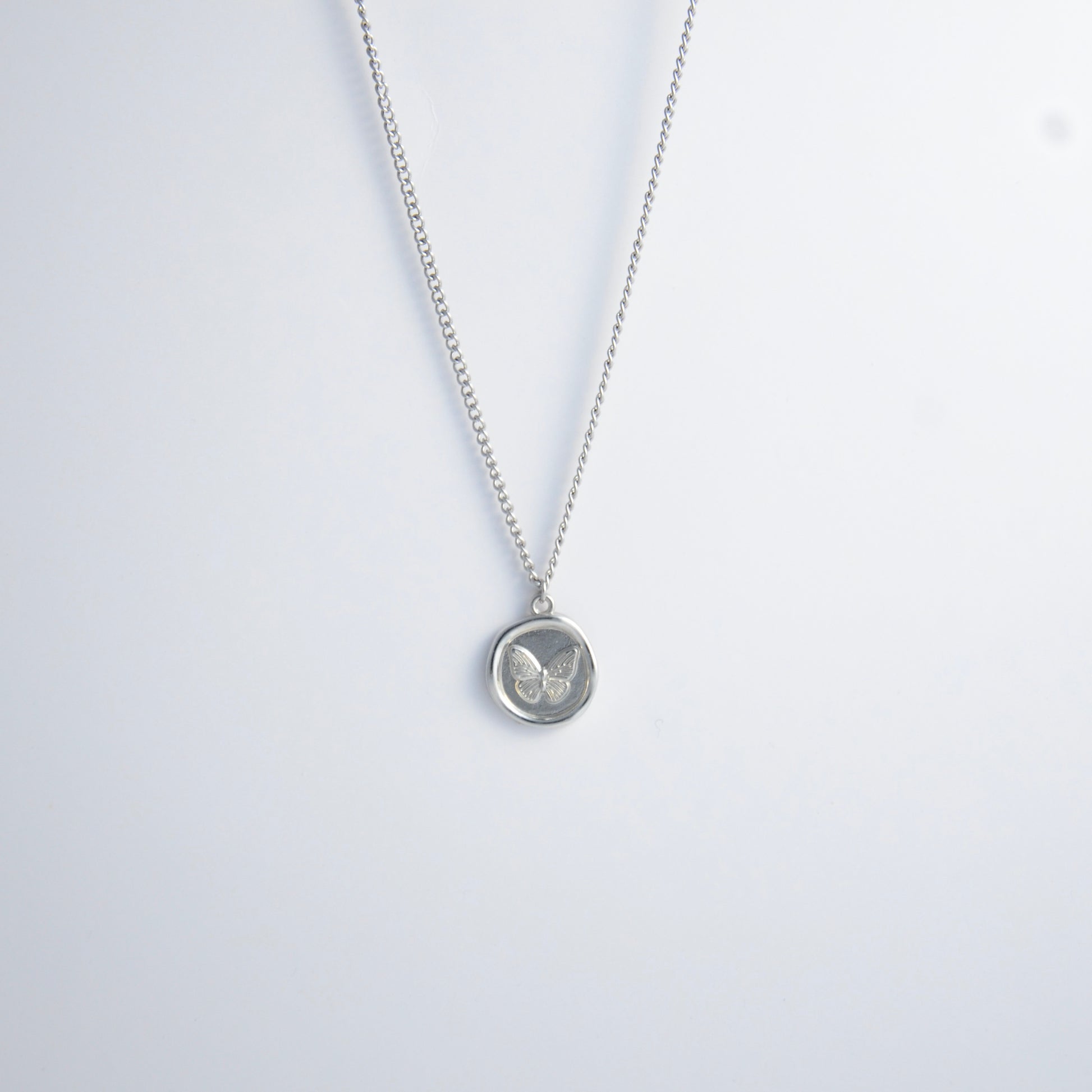 Silver curb necklace with a round butterfly pendant on a light gray background