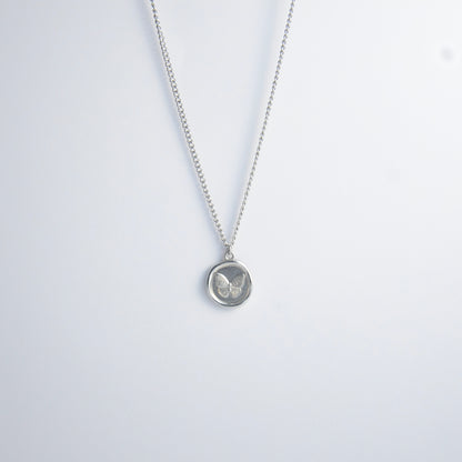 Silver curb necklace with a round butterfly pendant on a light gray background