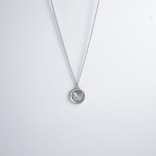 Silver curb necklace with a round butterfly pendant on a light gray background