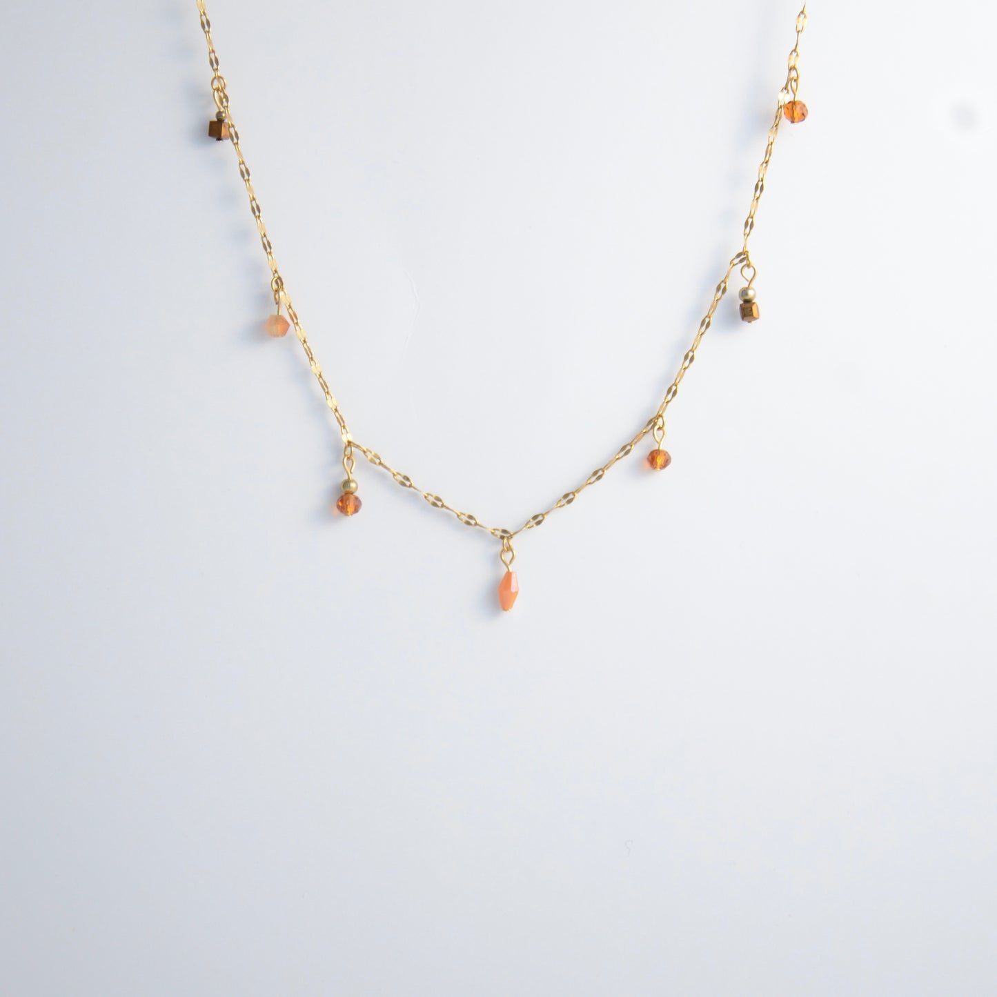 Delicate gold satellite necklace with small orange beads on a light gray background