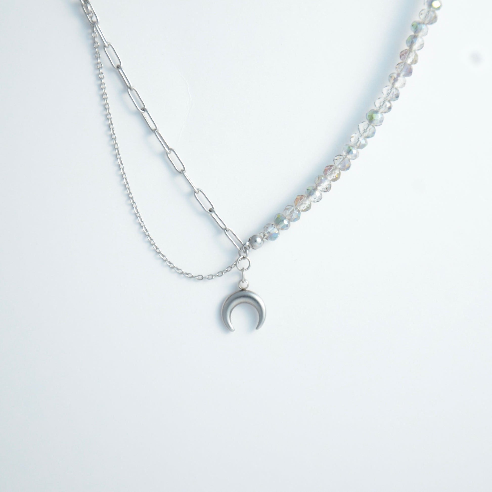 Silver layered necklace with a moon pendant and glass beads on a paperclip chain on a light gray background