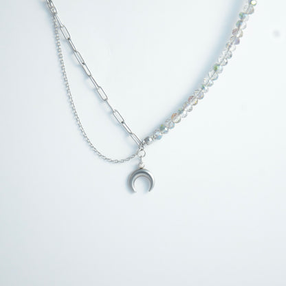 Silver layered necklace with a moon pendant and glass beads on a paperclip chain on a light gray background