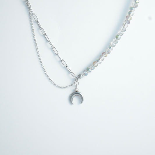 Silver layered necklace with a moon pendant and glass beads on a paperclip chain on a light gray background