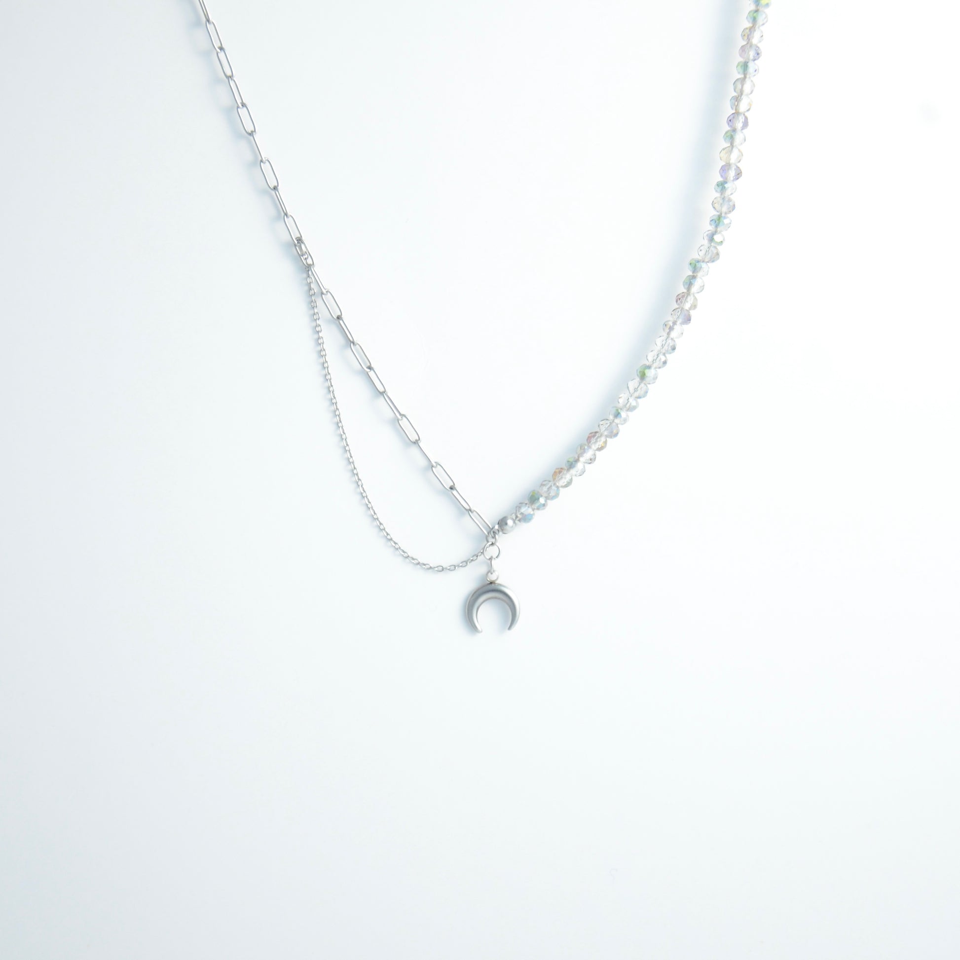 Silver layered necklace with a moon pendant and glass beads on a paperclip chain on a light gray background