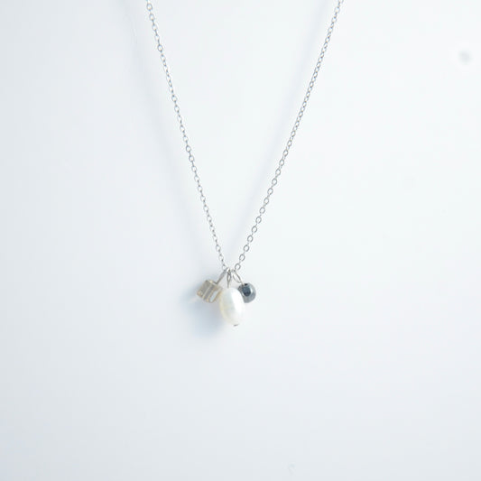 Silver dainty necklace with three small charms made of glass beads and pearls on a white background