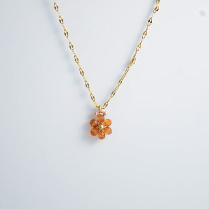 Gold necklace with a small orange flower pendant on a white background