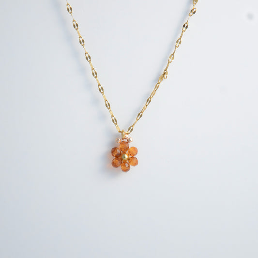 Gold necklace with a small orange flower pendant on a white background
