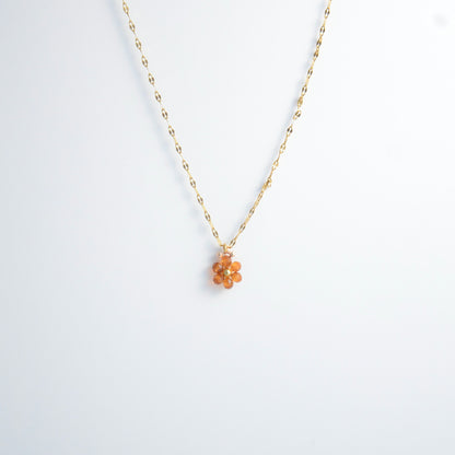 Gold necklace with a small orange flower pendant on a white background