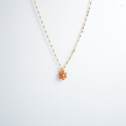 Gold necklace with a small orange flower pendant on a white background