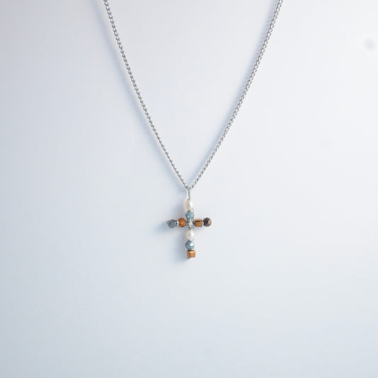 Silver curb chain necklace with a cross pendant made of freshwater pearls and blue, orange and black glass beads on a light gray background