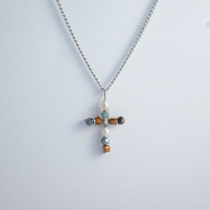Silver curb chain necklace with a cross pendant made of freshwater pearls and blue, orange and black glass beads on a light gray background