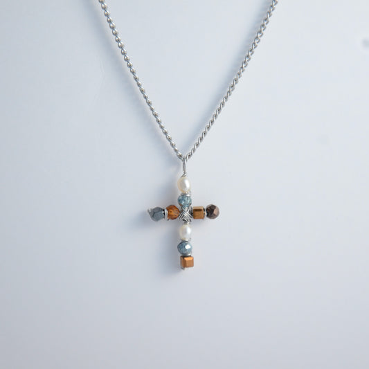 Silver curb chain necklace with a cross pendant made of freshwater pearls and blue, orange and black glass beads on a light gray background
