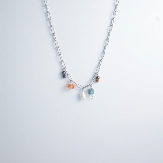Silver paperclip chain necklace with small bead charms including freshwater pearls, black, blue, and orange glass beads on a light gray background