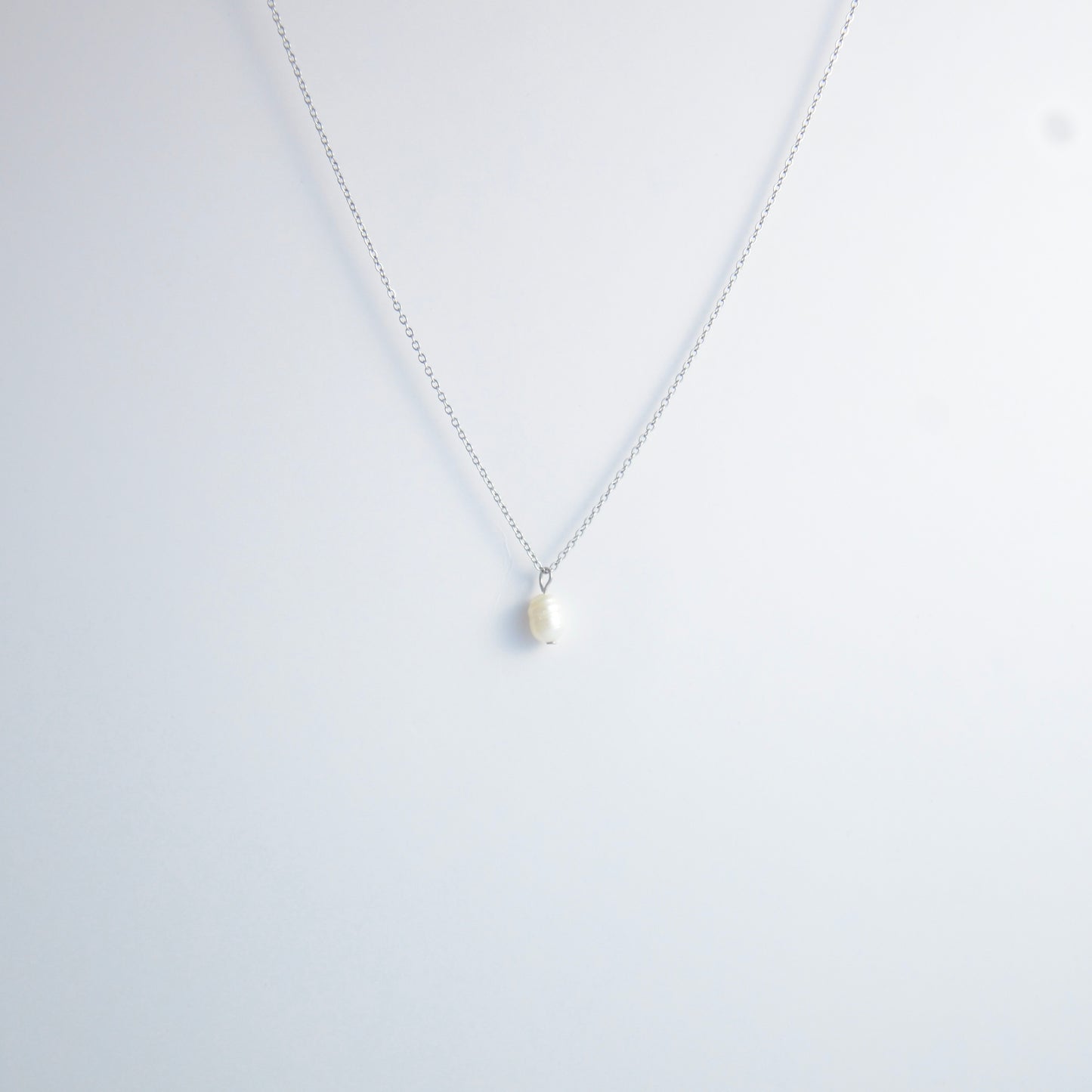 Silver dainty pearl necklace with freshwater pearl charm on a light gray background
