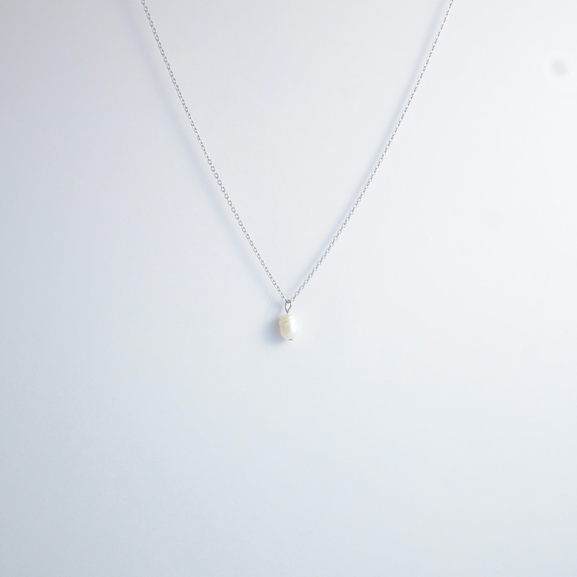 Silver dainty pearl necklace with freshwater pearl charm on a light gray background