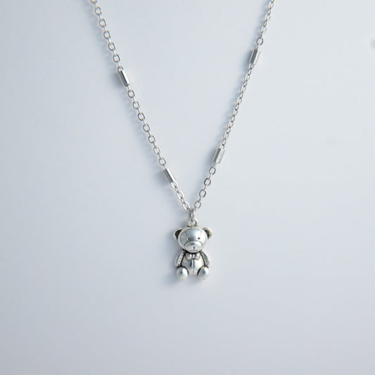 Dainty silver bar link chain with a teddy bear charm for minimalistic fashion or for layering jewelry on a light gray background